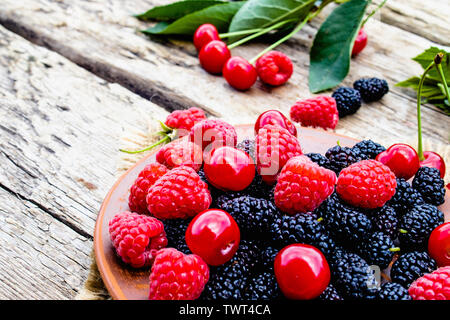mixed berries of raspberry, cherry, mulberry in a bowl on wooden background. Close-up Stock Photo