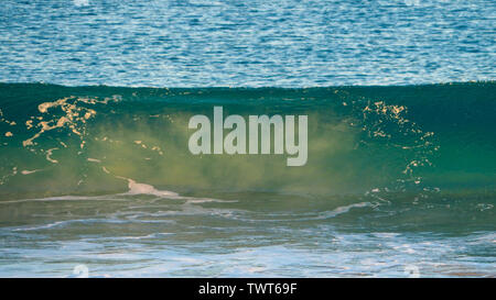 Natural patterns, front on to blue green ocean wave rolling in, with swept up sand in the waves, Forster NSW Australia Stock Photo