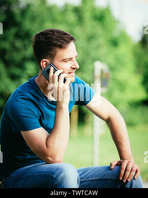 Handsome young man is sitting outdoors and talking with someone on the phone Stock Photo