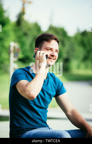 Handsome young man is sitting outdoors and talking with someone on the phone Stock Photo