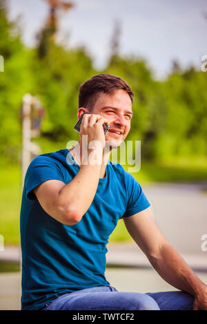 Handsome young man is sitting outdoors and talking with someone on the phone Stock Photo