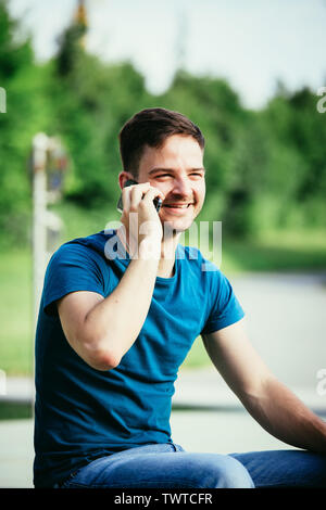 Handsome young man is sitting outdoors and talking with someone on the phone Stock Photo