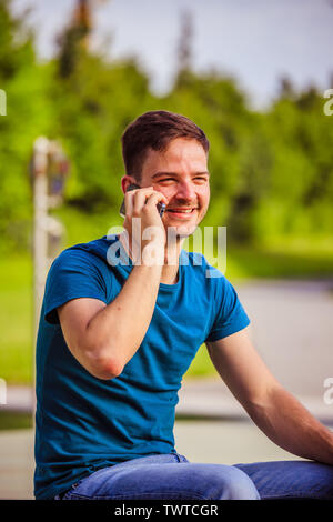 Handsome young man is sitting outdoors and talking with someone on the phone Stock Photo