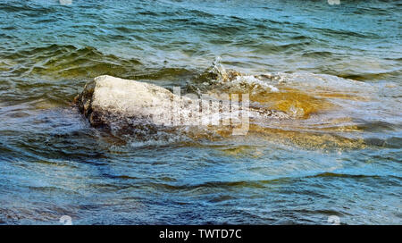 Beautiful lake waters of blue and green crashing up against large rocks Stock Photo