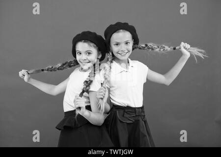 Loving their new style. Small children with long hair plaits. French style  girls. Cute girls having the same hairstyle. Fashion girls with tied hair  into braids. Little kids wearing french berets Stock