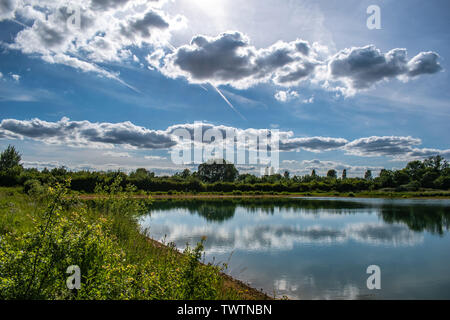 The cloudy sky above is reflected in the still waters of a lake below. Taken in Oxfordshire, England.