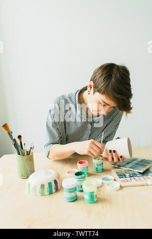 the pottery woman holds in hands a mug to paint the ornament, handmade ceramic Stock Photo