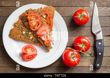 Rustic raw food preparation concept. Healthy nutrition background. Vegan dried bread, sliced and whole tomatoes and knife laid on oak wooden kitchen t Stock Photo