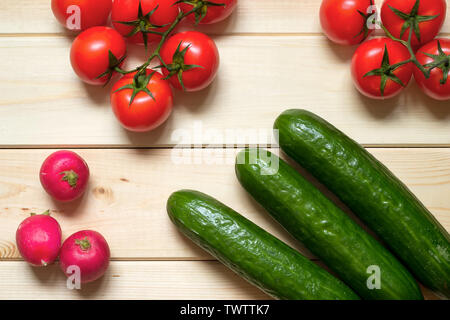 Fresh ripened vegetables background. Radishes, cucumbers and tomatoes on light wooden table. Top view. Close-up. Harvested raw food. Healthy nutrients Stock Photo