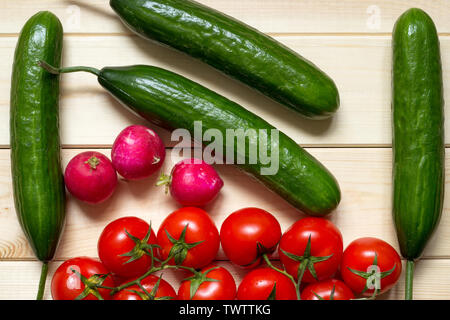 Natural food background with cucumbers, tomatoes and radishes. Ripened vegetables laid out on light wooden table. Top view. Close-up. Fresh raw foods. Stock Photo