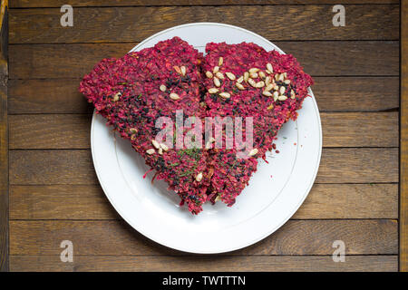Vegan dry bread loaves, cooked from beetroot, walnuts, garlic and seeds by low baking in dehydrator, stacked on white plate on wooden table. Raw foods Stock Photo