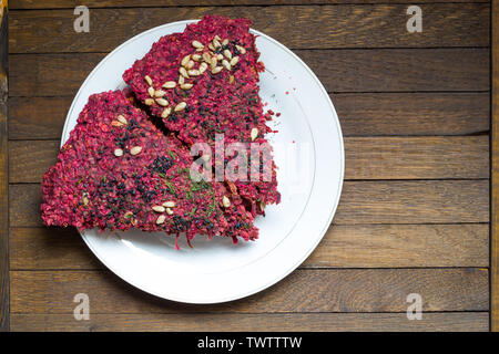 Vegan dry bread loaves, cooked from beetroot, walnuts, garlic and seeds by low baking in dehydrator, stacked on white plate on wooden table. Copy spac Stock Photo