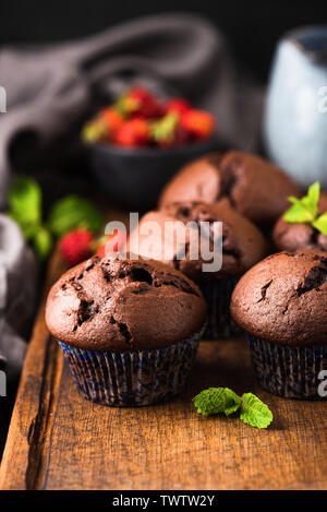 Dark chocolate muffins on wooden board. High in calories, sugar and gluten food. Unhealthy food. Warm tones Stock Photo