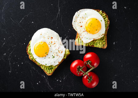Sunny side up egg and avocado on whole grain toasted bread on black marble table background. Top view Stock Photo