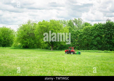 red tractor with lawn mower mows the lawn in the Park, lawn Mower mows the grass Stock Photo