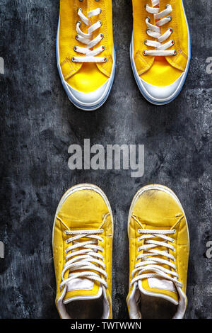 yellow old worn dirty torn sneakers and and new sneakers on a dark grunge background. top view. Copy space Stock Photo