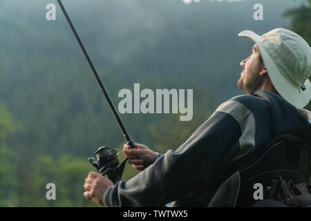 young man in a wheelchair fishing at the beautiful lake in sunset, dawn. Looking at fish that he caught Stock Photo