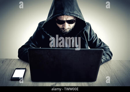 Hacker data steeling information man with hoodie sitting on desk with laptop Stock Photo