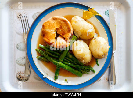Tasty Yorkshire meal steak pie with new potatoes  Asparagus gravy and mustard blue edged plate on a tray Stock Photo