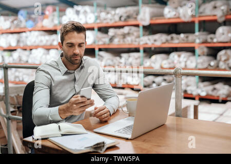 Warehouse manager checking his cellphone while working in his office Stock Photo