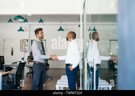 Two smiling businessmen shaking hands together after an office meeting Stock Photo