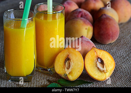 Fresh peaches and two glasses of freshly made peach juice on a sackcloth background Stock Photo