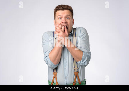 Young man in shirt and suspenders covering mouth with hands in shock Stock Photo