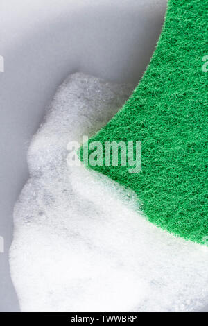 A hand with a green sponge washes a gray ceramic plate with detergent foam. On a wooden table. Vertical view Stock Photo