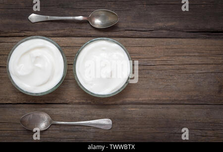 White yogurt in two glass bowls on old wooden desk with two spoons next to. Stock Photo