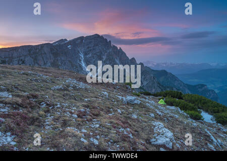 Wild camping at sunset on a mountain top, pink sky, colorful clouds. Darkening sky with alpenglow, lone Berghaus tent pitched on the mountainside. Stock Photo