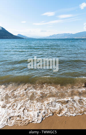 Waves rolling onto Okanagan Beach with view of Okanagan Lake, mountains, and blue sky Stock Photo