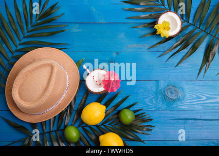 Tropical summer background with hat, palm leaves, lemons, lime, coconuts on blue wooden table Stock Photo