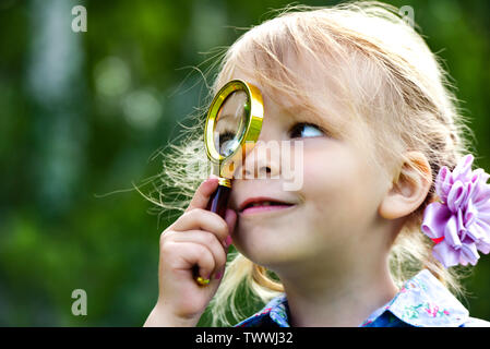 The child looks through a magnifier. Beautiful little girl looking through a magnifying glass. Stock Photo