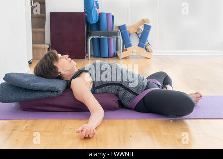 a 70 year old yoga instructor in her studio does  Reclining Bound Angle Pose , aka Supta Baddha Konasana, a restorative relaxation pose. Inversion str Stock Photo