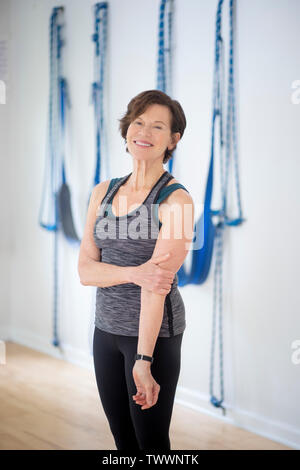 a 70 year old yoga instructor in her studio stands for a portrait in front of a wall with yoga  wall ropes Stock Photo