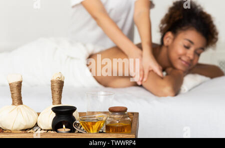 Afro Woman Relaxing In Spa Salon With Herbal Bags on Foreground Stock Photo