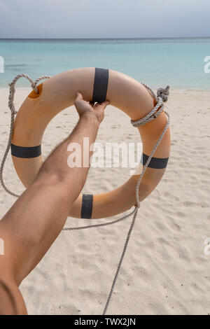 Male hand holding a life preserver. In the background sand, sea and sky Stock Photo