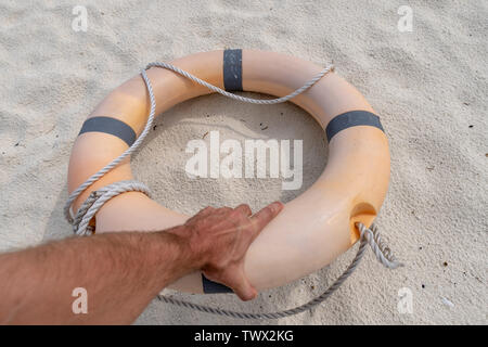 Male hand holding a life preserver. In the background sand Stock Photo