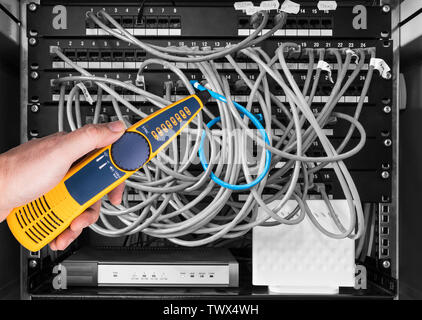 Network cable tester detail. Measuring probe in hand of expert. Diagnostic measurement of structured cabling in patch panels of rack case. IT service. Stock Photo