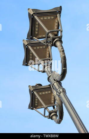 photo of three modern metal lamps in vintage style on a single post against a blue sky Stock Photo