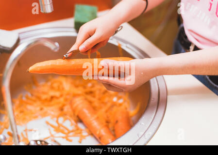 The girl cleans carrots from dirt and skins in the sink under the faucet. cleaning carrots in the sink. man prepares a dish of carrots Stock Photo