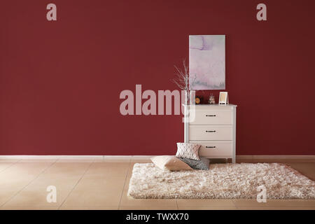 Chest of drawers with stylish decor and pillows near color wall in room Stock Photo