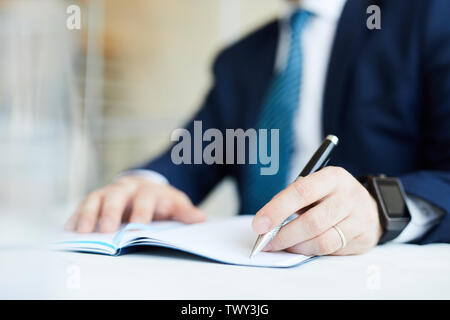 Close-up of unrecognizable businessman in suit sitting at table and making notes in diary while setting tasks for business Stock Photo