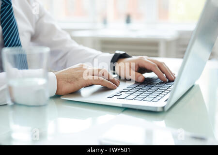 Close-up of unrecognizable businessman in white shirt sitting at table and using laptop for business analysis Stock Photo
