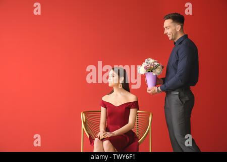 Offended young woman refusing to take bouquet of beautiful flowers from her boyfriend on color background Stock Photo