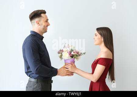 Woman receiving flowers from young man on light background Stock Photo