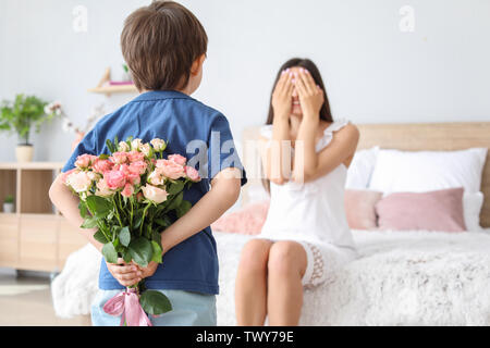 Little boy hiding bouquet of flowers for his mother behind back at home Stock Photo