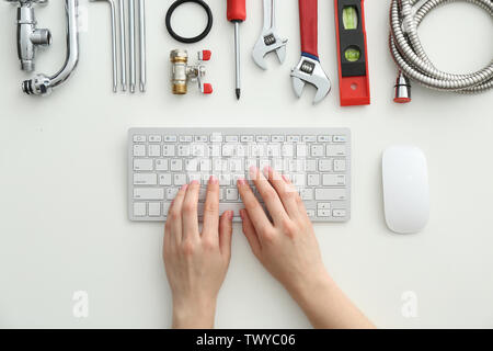 Plumbing tools and woman with computer keyboard on white background, top view Stock Photo