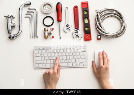 Plumbing tools and woman with computer keyboard on white background, top view Stock Photo