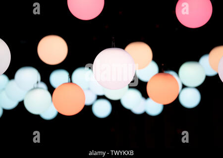Colored round globe pendant lights suspended, form a random pattern on a dark background, blurred in the distance. Pink, orange, peach and blue color. Stock Photo